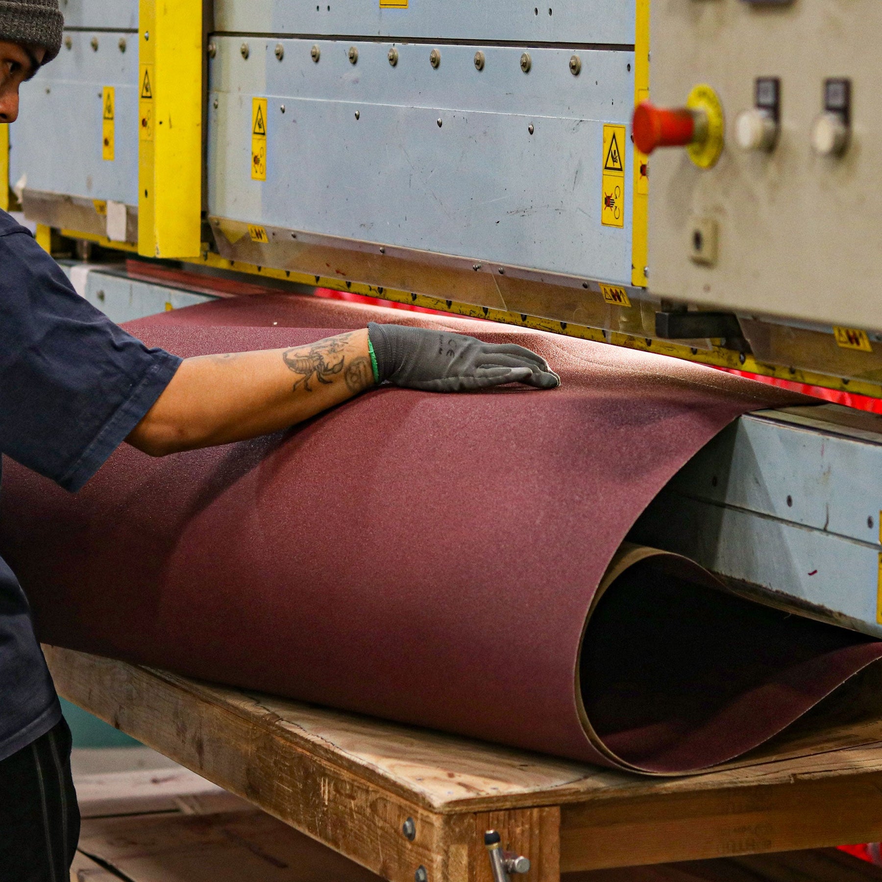 Worker handling a wide sanding belt at an industrial belt-converting machine