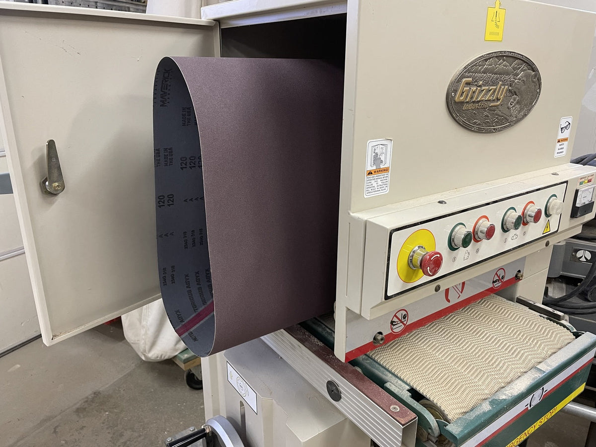 Wide abrasive belt hanging from the open hood of a Grizzly wide belt sander