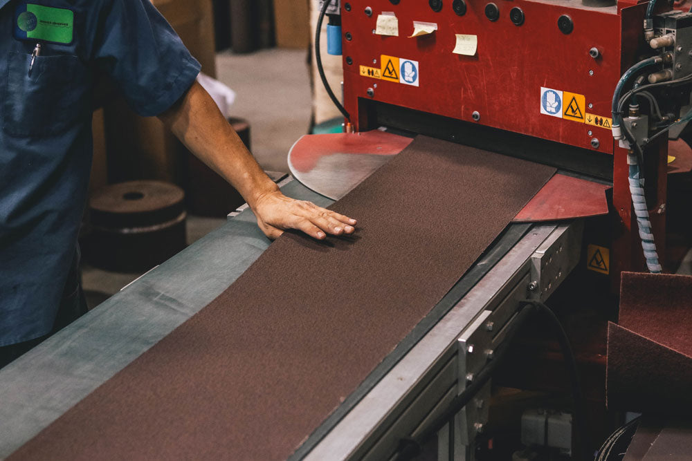 Worker feeding wide abrasive material through a belt-converting machine