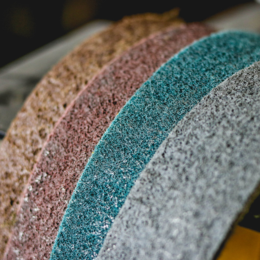 Assorted 4x36 non-woven surface conditioning belts in brown, maroon, blue, and grey for metal finishing.